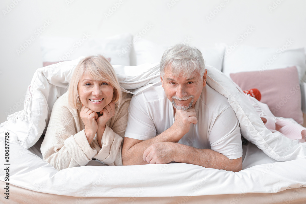 Happy mature couple lying under blanket in bed