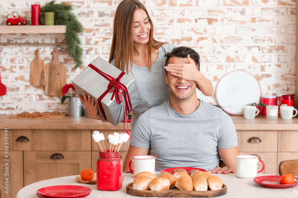 Happy young woman giving Christmas present to her boyfriend at home