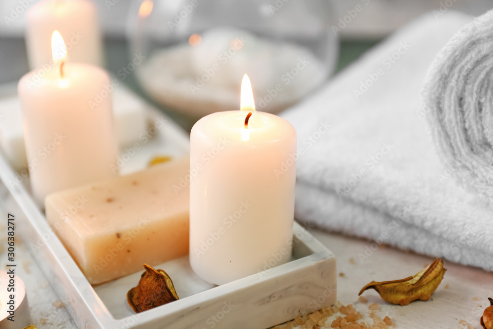 Glowing candles with soap and towel on table