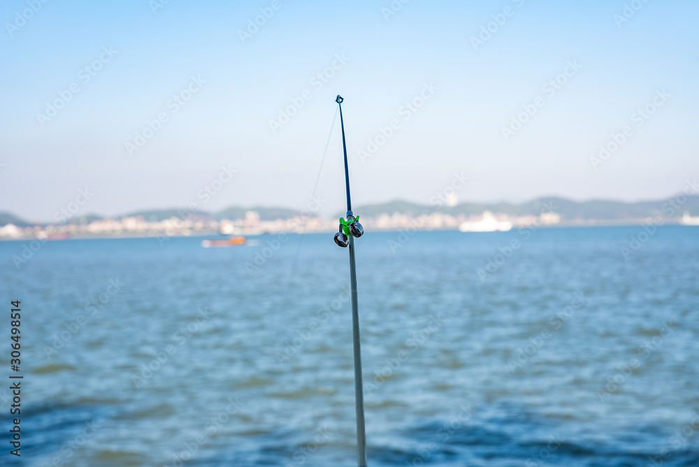 A fishing rod is set up by the coast under the blue sky