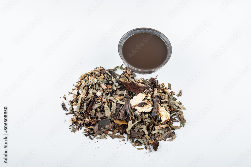 A pile of Chinese herbs and a bowl of boiled medicinal soup on white background