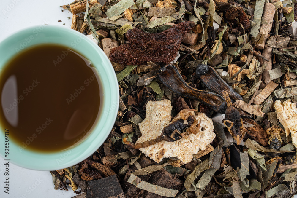 A pile of Chinese herbs and a bowl of boiled medicinal soup on white background