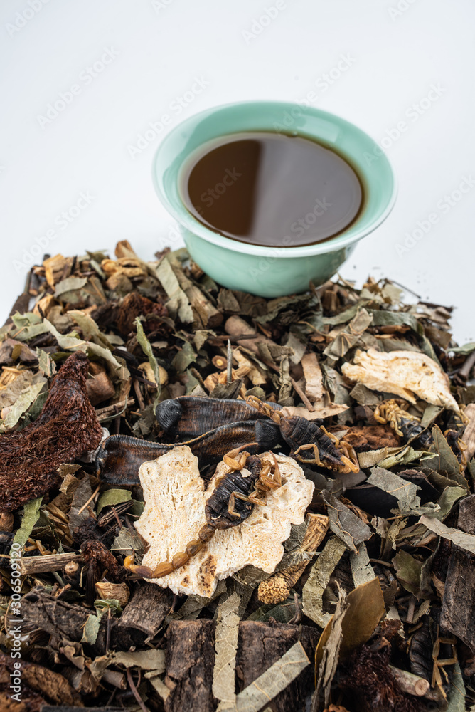 A pile of Chinese herbs and a bowl of boiled medicinal soup on white background