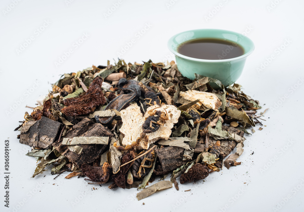 A pile of Chinese herbs and a bowl of boiled medicinal soup on white background