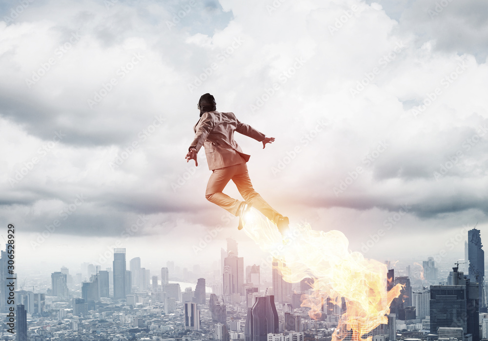 Businessman in suit and aviator hat flying in sky