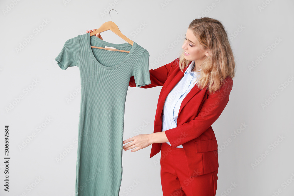 Female worker of modern dry-cleaner with clothes on light background