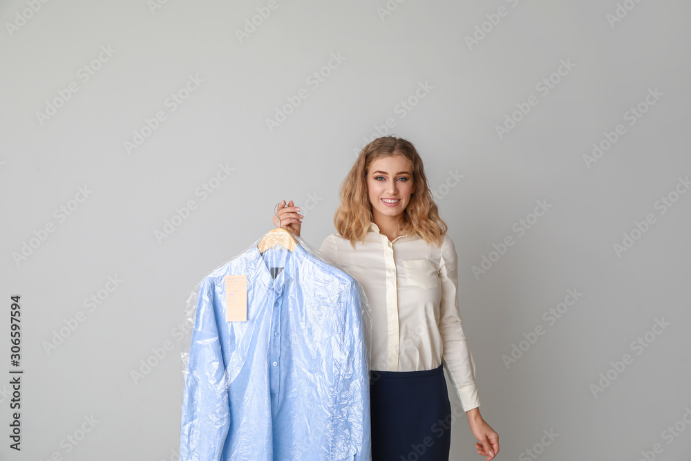 Female worker of modern dry-cleaner with clothes on light background