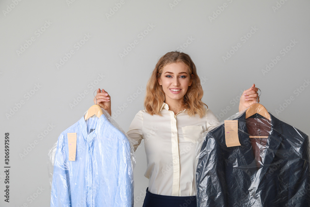 Female worker of modern dry-cleaner with clothes on light background