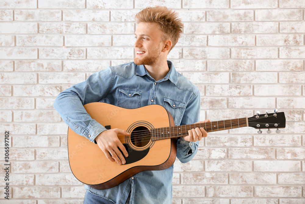 Handsome man with guitar against brick wall