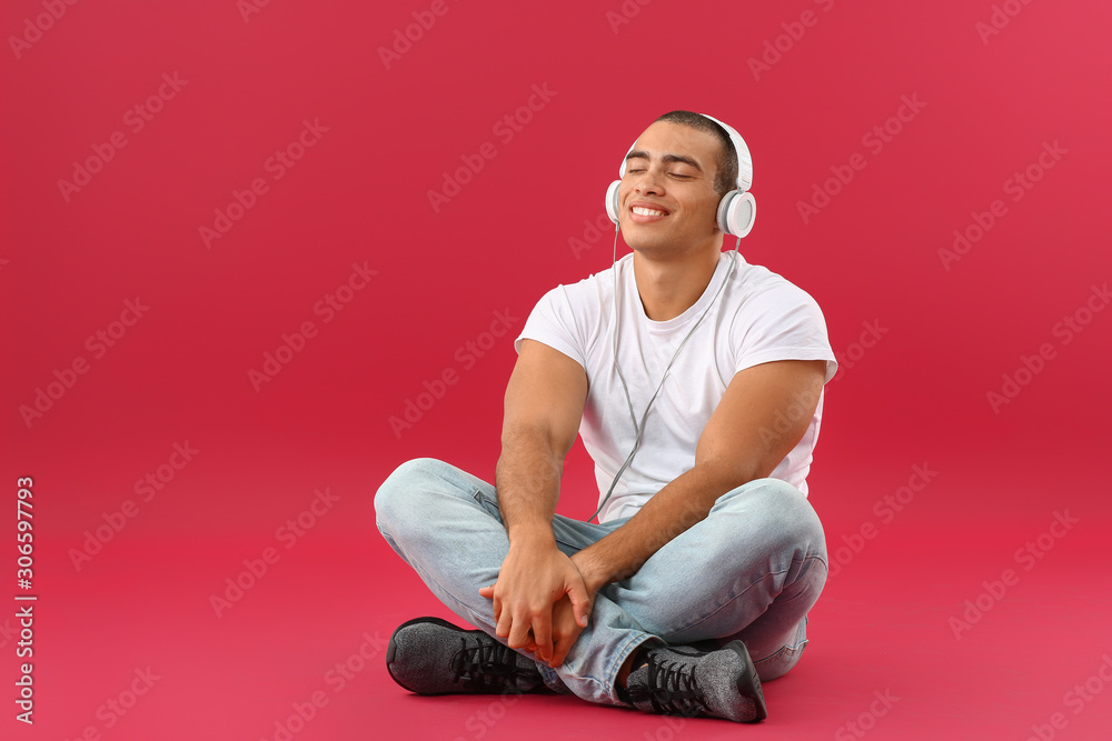 Portrait of handsome young man listening to music on color background