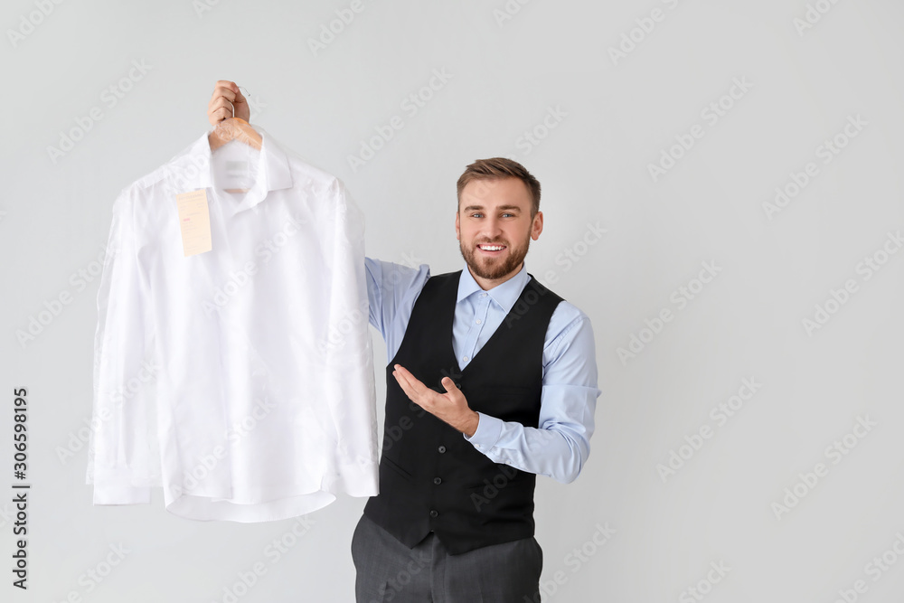 Male worker of modern dry-cleaners with clothes on light background