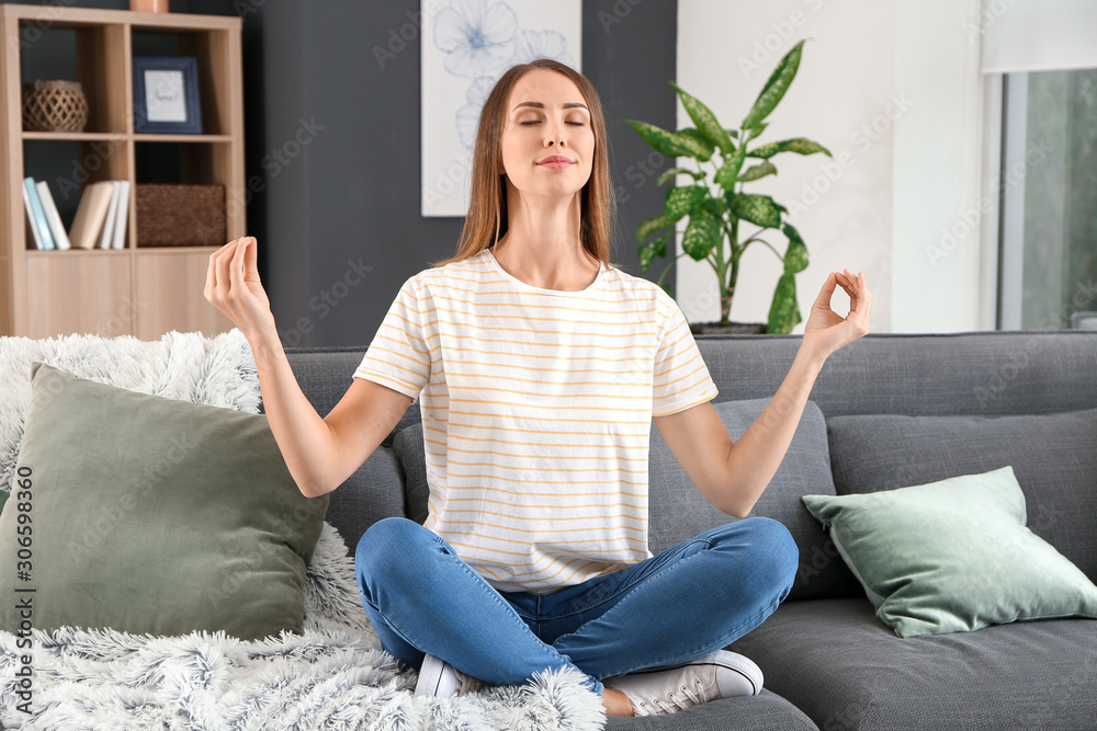 Beautiful young woman meditating at home