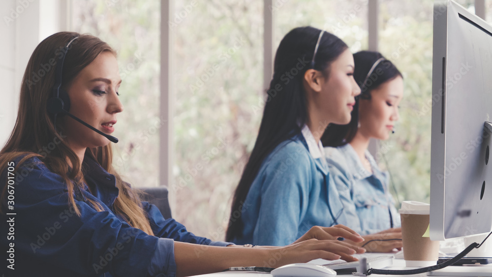 Customer support agent or call center with headset works on desktop computer while supporting the cu