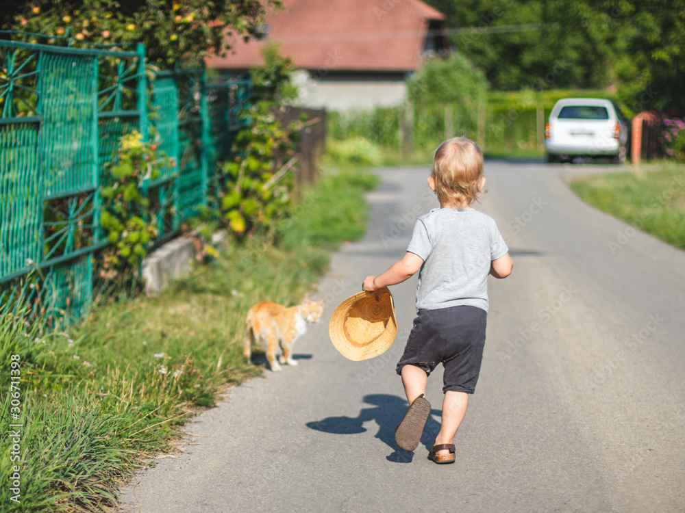 Child boy with his cat walking together on path near house