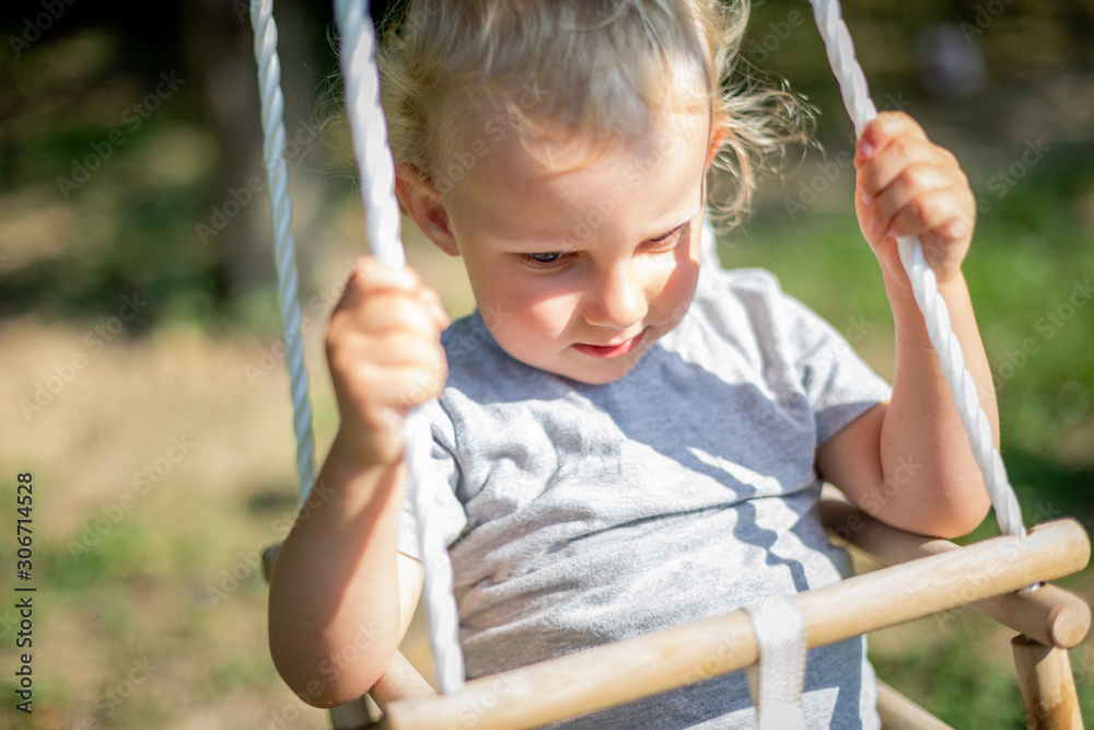 Happy small child sitting in baby swing outdoor in backyard