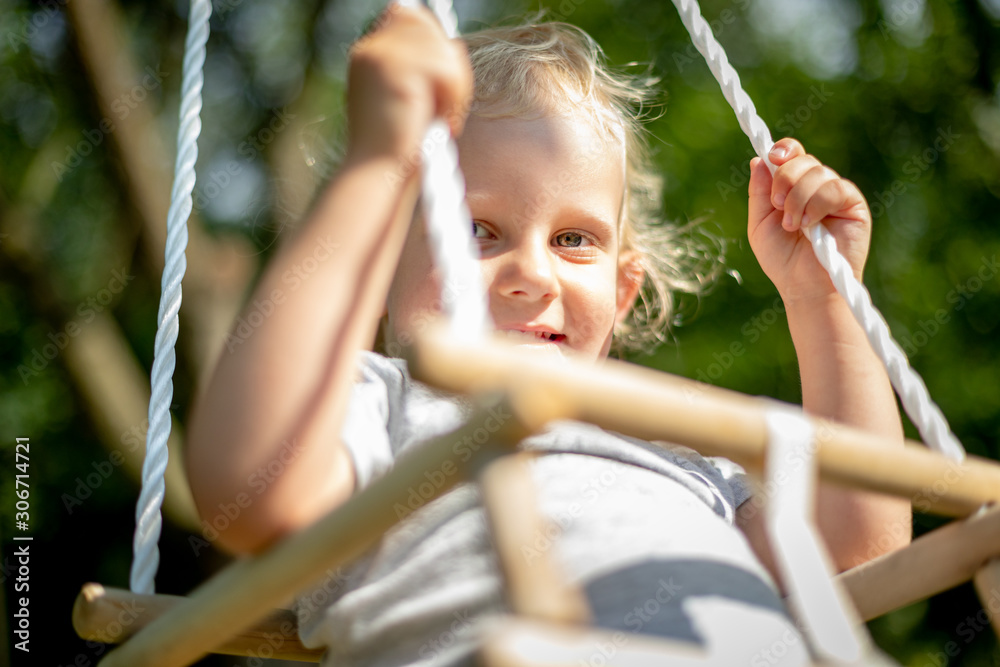 Happy small child sitting in baby swing outdoor in backyard