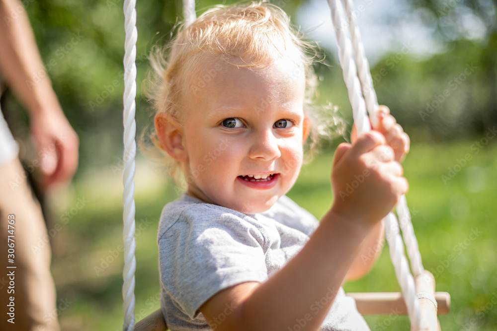 Happy small child sitting in baby swing outdoor in backyard