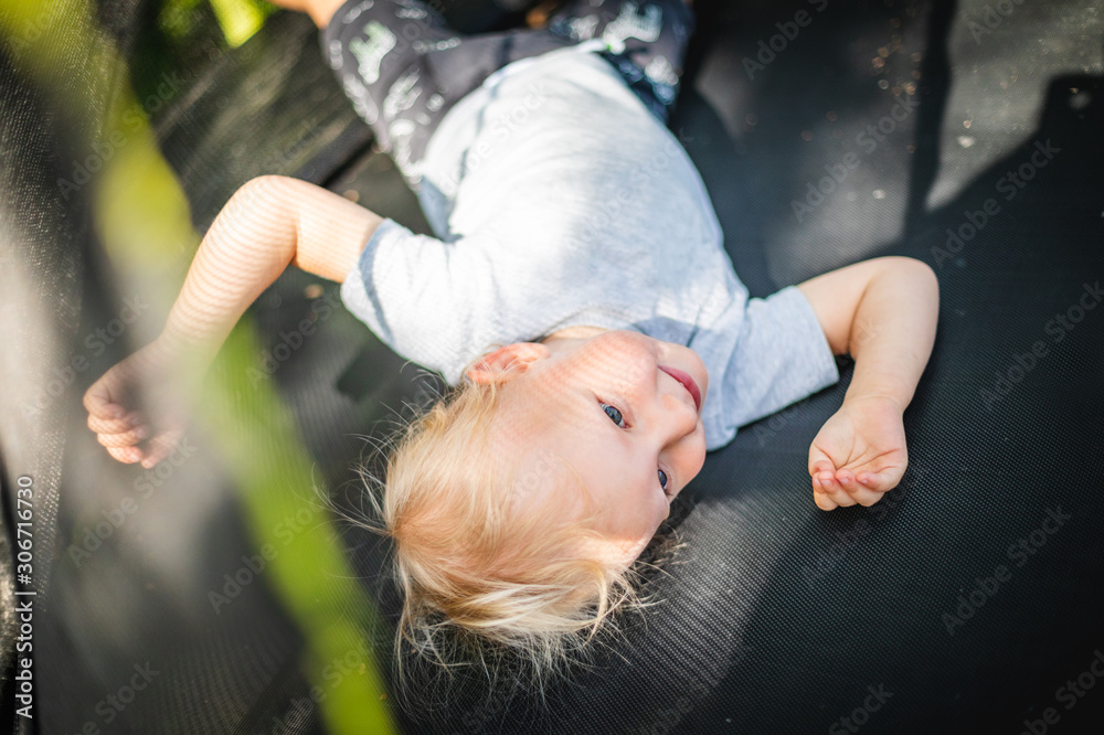 Little child playing and jumping on trampoline outdoor in backyard