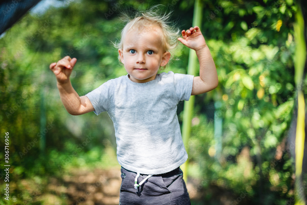 Little child playing and jumping on trampoline outdoor in backyard