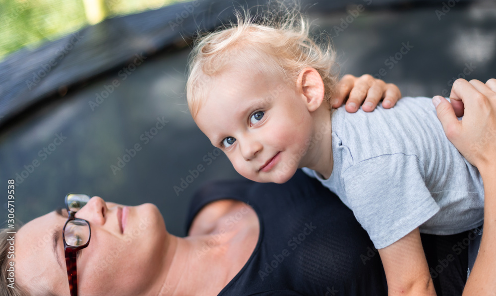 Little child with his mom laying on trampoline outdoor in backyard