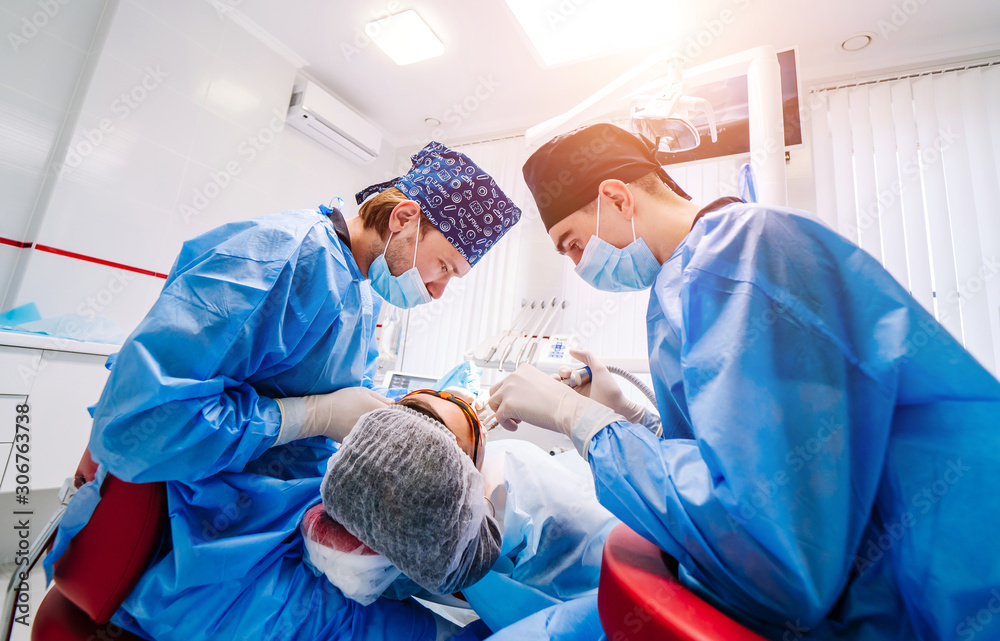 Two male dentist in uniform perform dental implantation operation on a patient at dentistry office, 