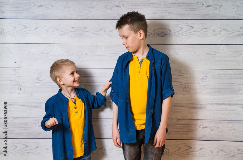 Two boys in casual clothes in white wooden background looking at each other. Two brothers posing. El