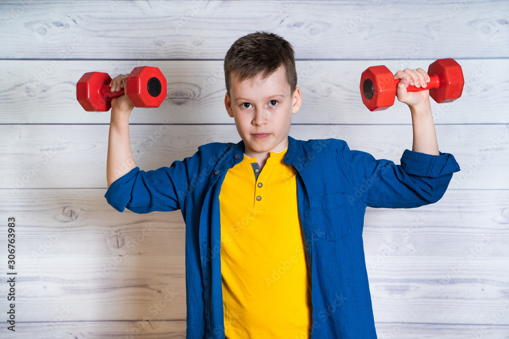 young boy in casual clothes with dumbbells in a studio. Boy leads a healthy lifestyle. Teen going sp