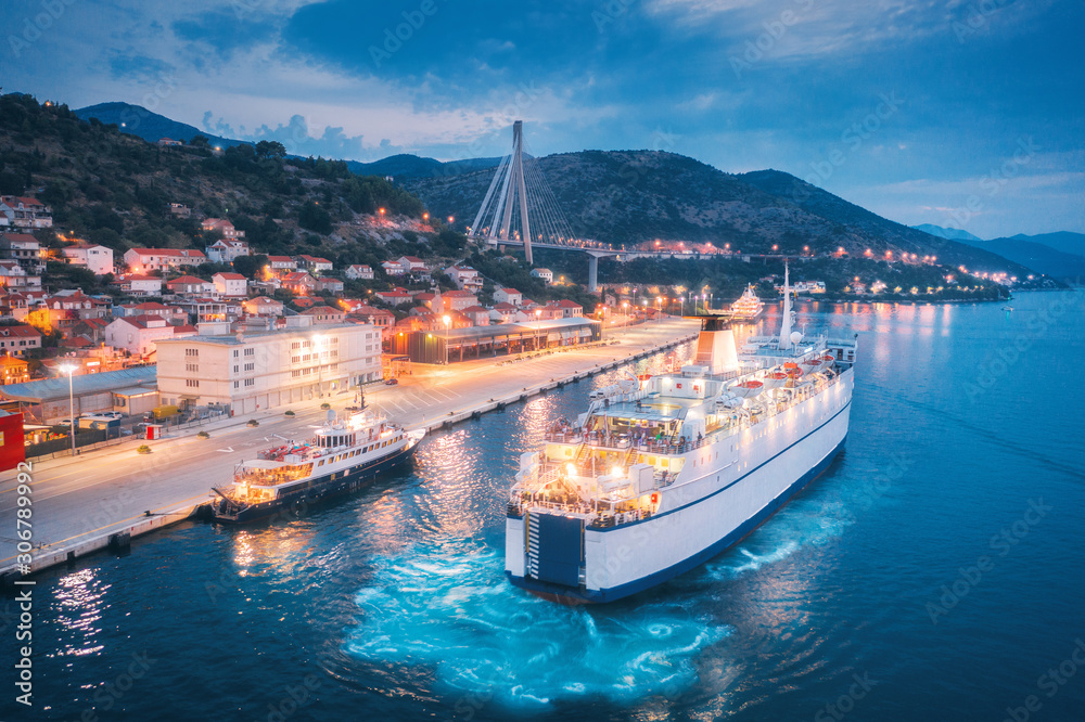 Aerial view of cruise ship in port at night. Landscape with ships and boats in harbour, city lights,