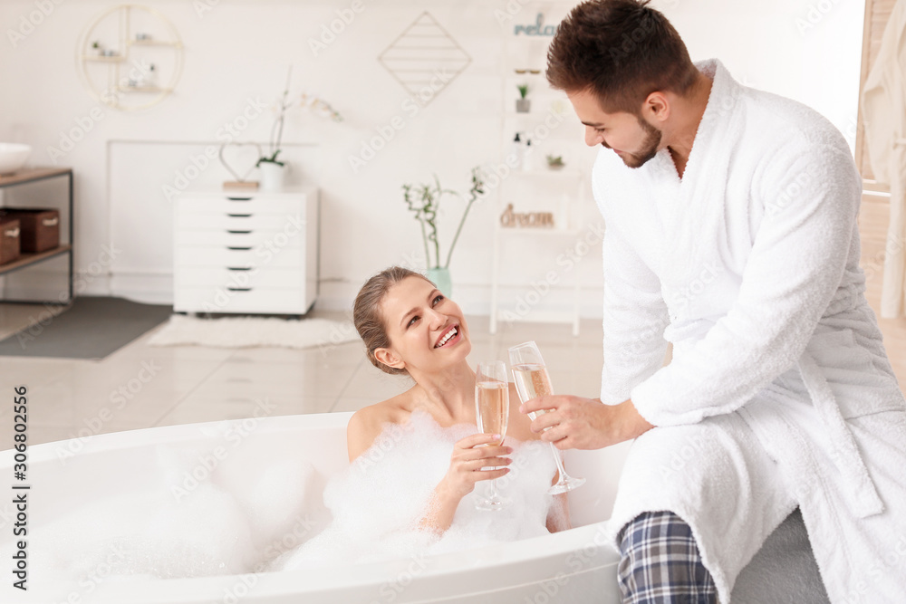 Happy young couple drinking champagne in bathroom