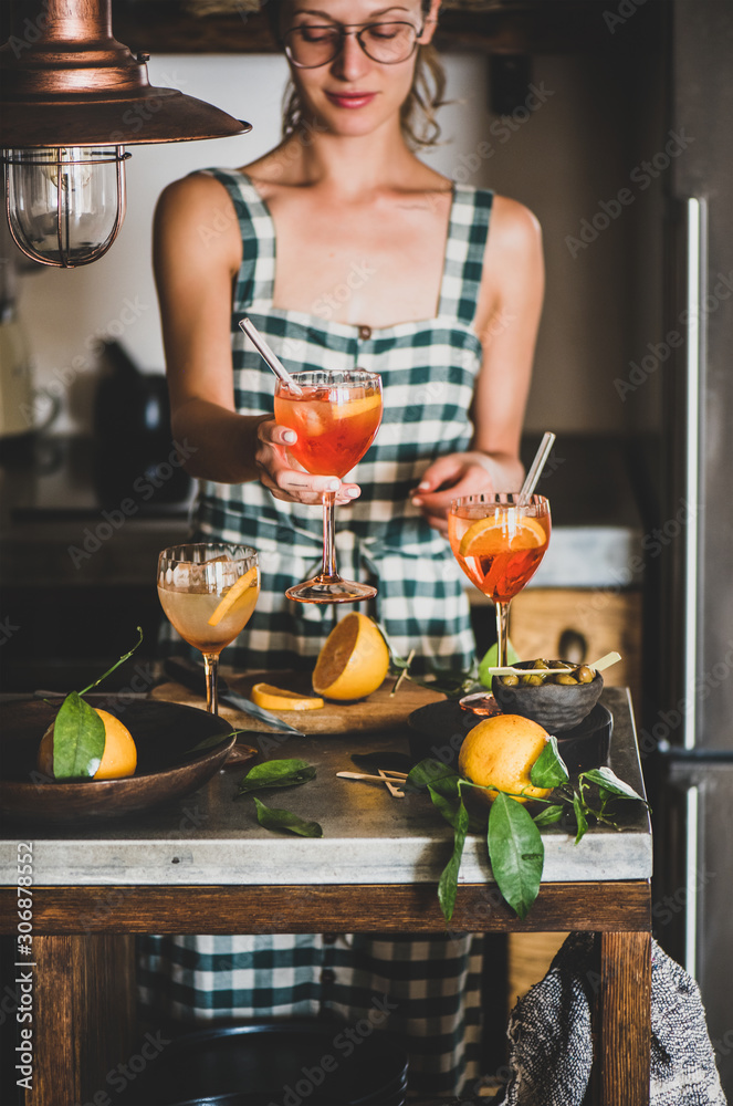 年轻的微笑女人，穿着格子连衣裙，手里拿着Aperol雪碧开胃酒，手里拿着橙，ki