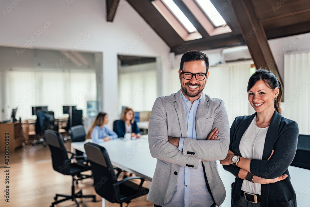 Portrait of two business partners standing with arms crossed in meeting room.