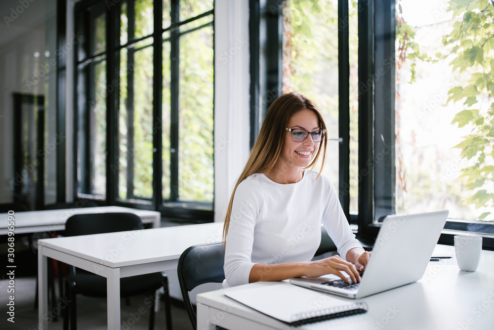 Beautiful young woman using laptop in modern co-working space.