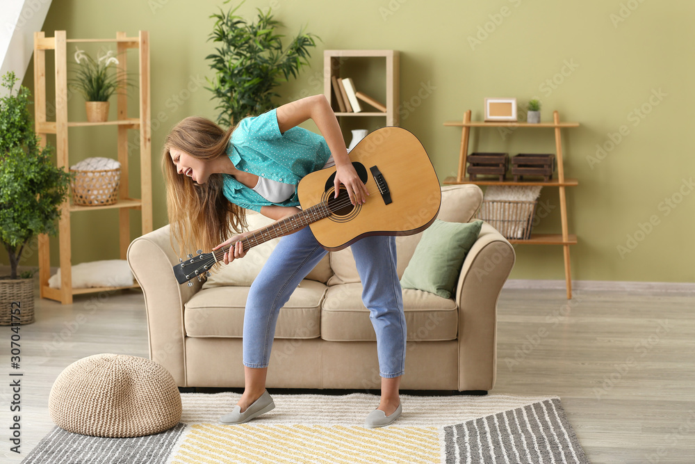 Beautiful young woman playing guitar and singing at home