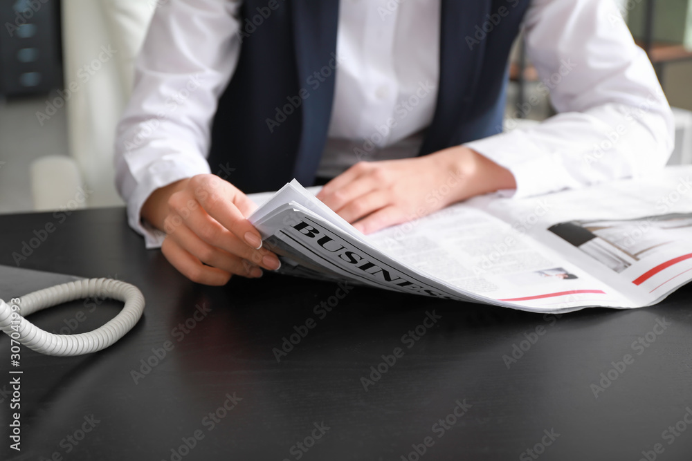 Young businesswoman reading newspaper in office