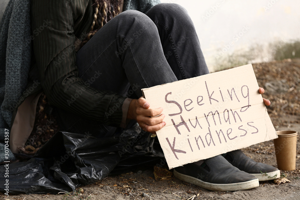 Poor homeless man holding cardboard with text SEEKING HUMAN KINDNESS outdoors