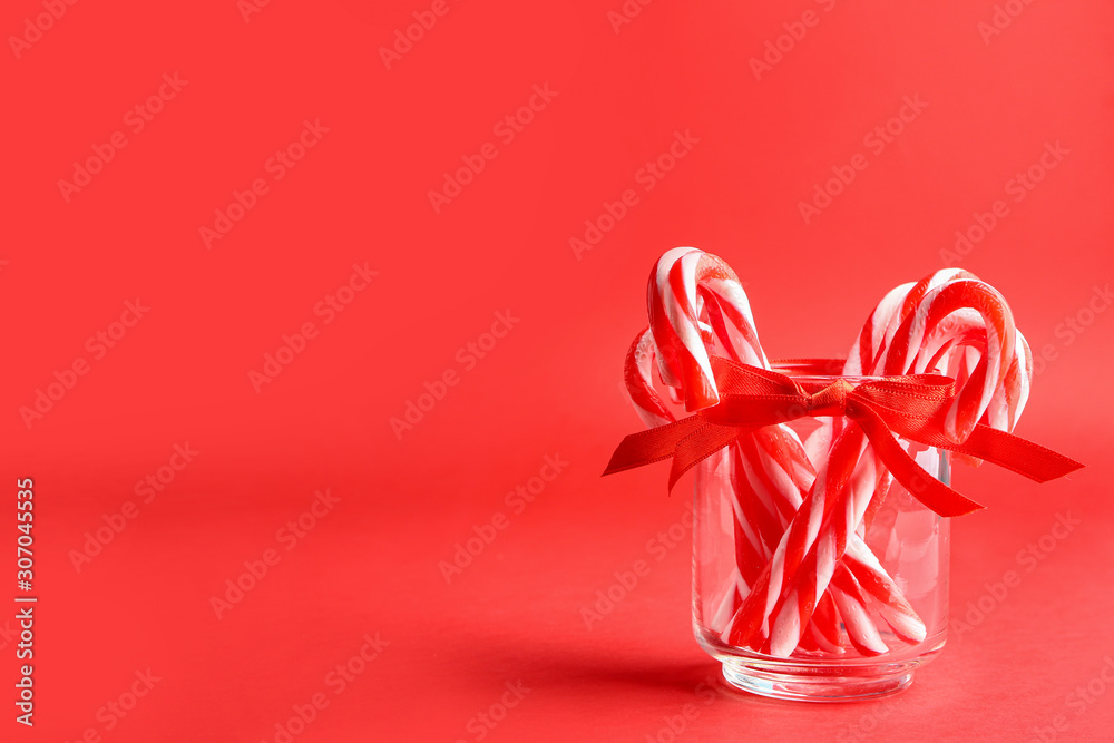 Glass with Christmas candy canes on color background