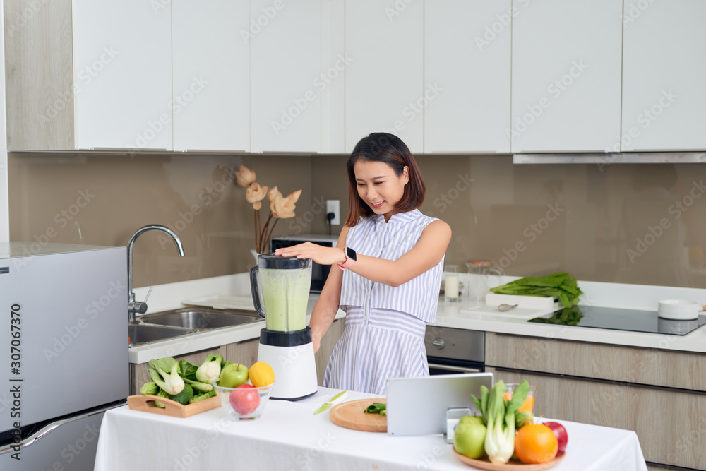 Beautiful Asian Woman juicing making green juice with juice machine in home kitchen. Healthy concept