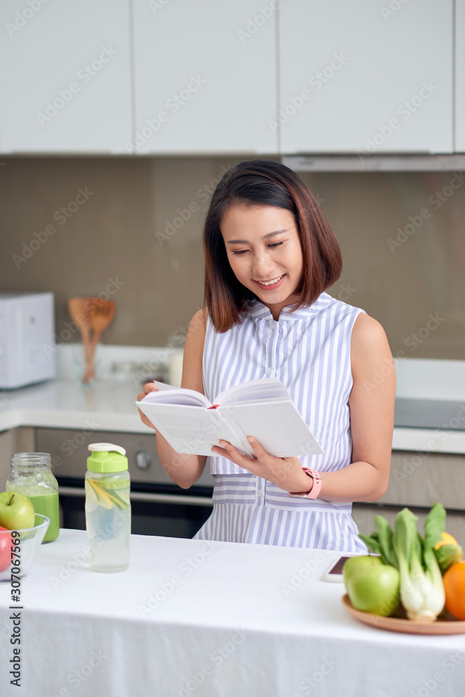 Pretty woman reading recipe to make detox drink in kitchen.