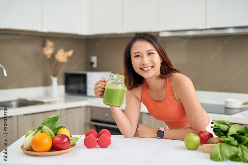 漂亮的亚洲女人穿着运动服喝排毒果汁