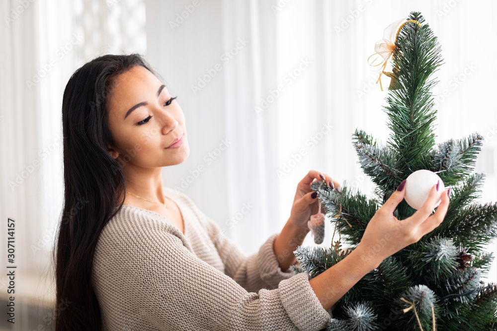 Young Asian woman decorating Christmas tree at home