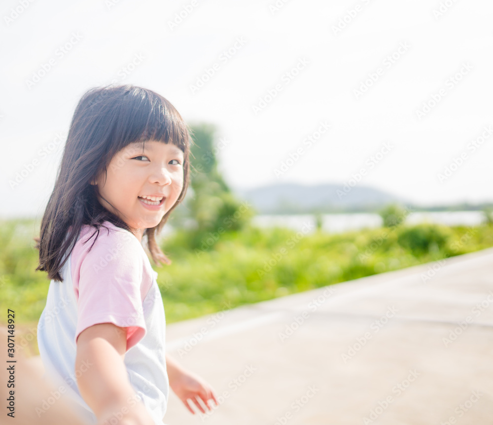 Happy Little asian girl child showing front teeth with big smile, laughing and jogging in summer par