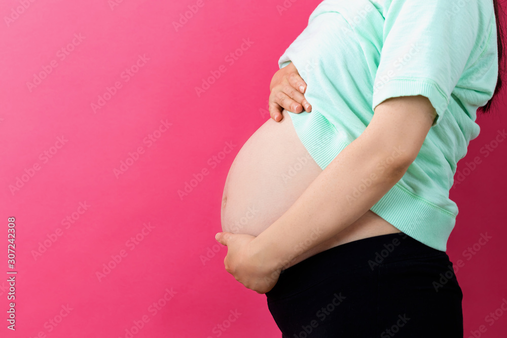 Pregnant woman on a solid background holding her belly