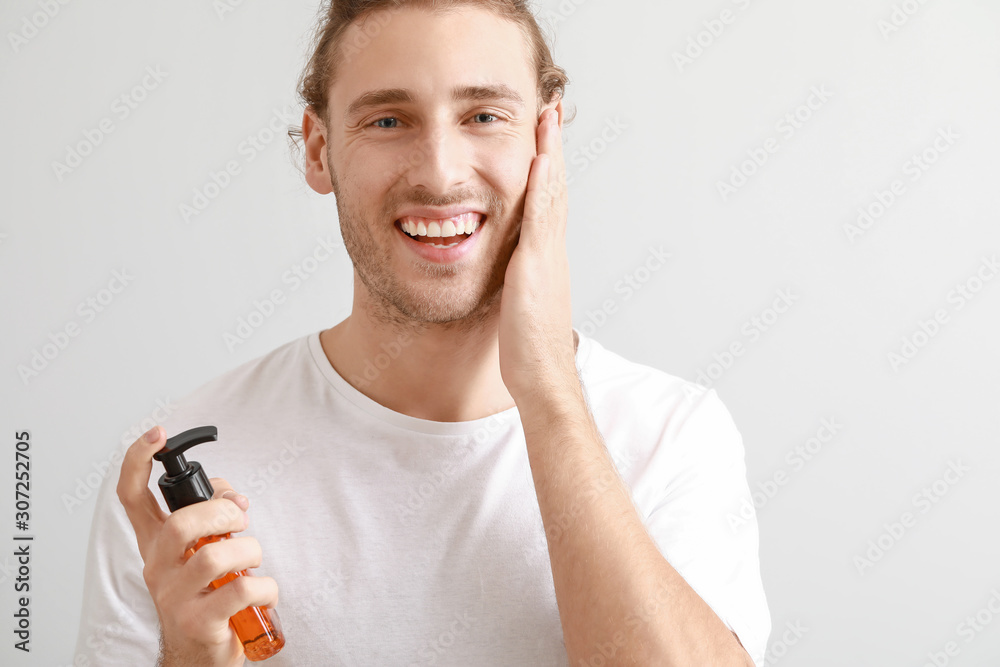 Handsome young man with cosmetic product on light background