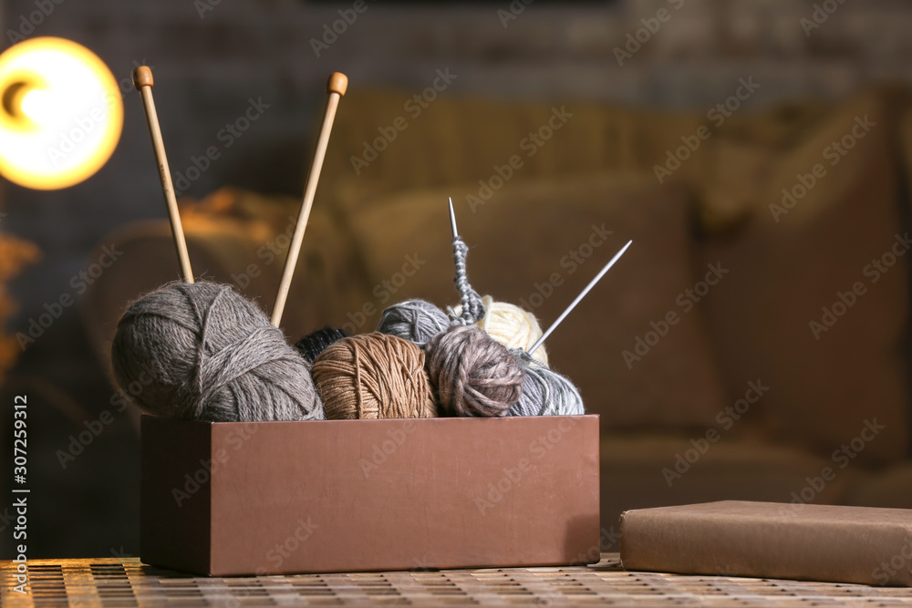 Box with knitting yarn and needles on table in room