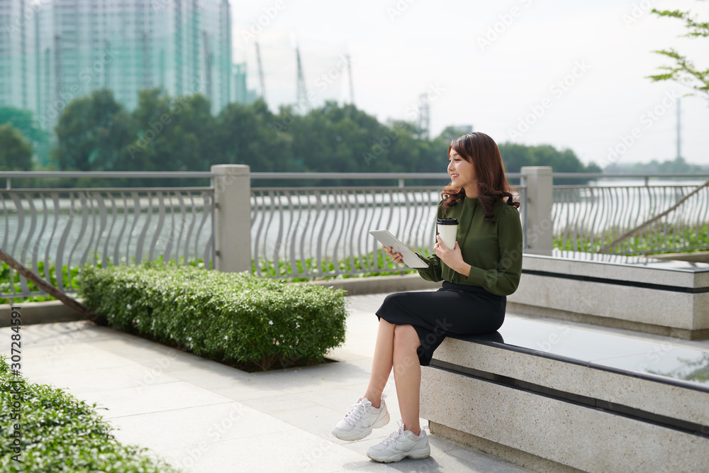 美丽的年轻女子在公园里使用平板电脑，笑容美丽