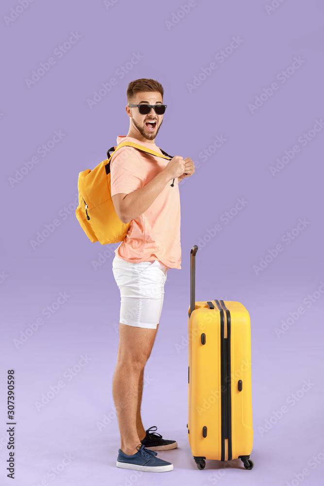 Young male tourist with luggage on color background