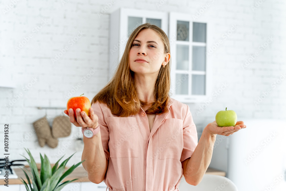 Portrait Of Young Girl standing on kitchen background. beautiful woman holding green apple and orang