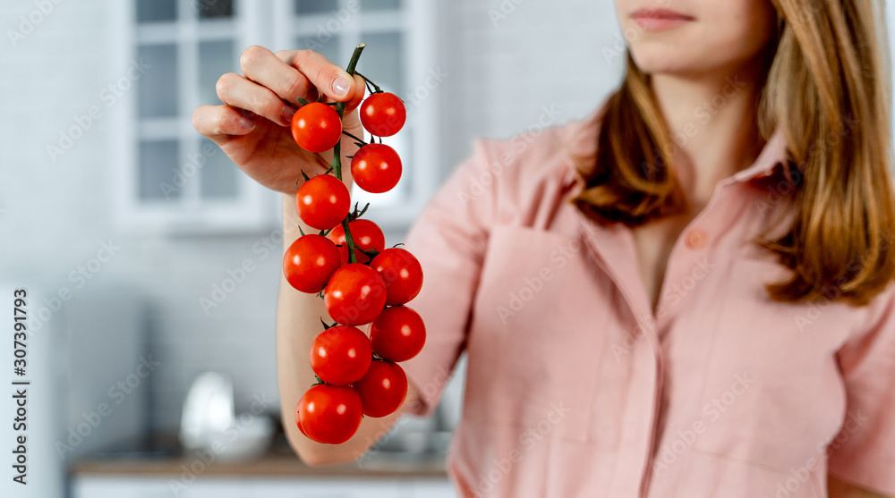 Woman in pink dress is holding branch of ripe cherry tomatoes, closeup