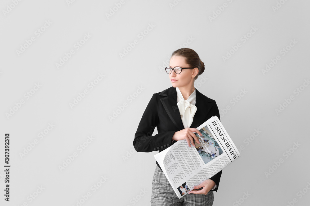 Young businesswoman with newspaper on light background