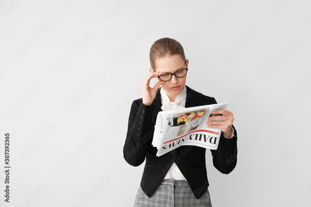 Young businesswoman with newspaper on light background